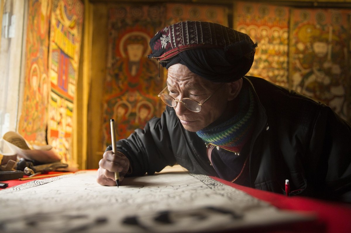 Artisan en pleine création dans un atelier traditionnel en Asie – Transmission culturelle et art local Artisan asiatique concentré sur une peinture traditionnelle dans un atelier décoré de fresques religieuses, illustrant la richesse culturelle locale.