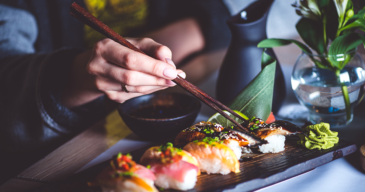 Dégustation de sushi dans un restaurant traditionnel au Japon Main tenant des baguettes en bois, dégustant des sushis variés dans un cadre japonais raffiné avec sauce soja, wasabi et décor floral