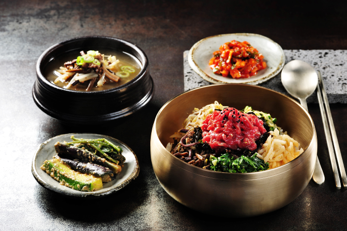 Bibimbap traditionnel et spécialités coréennes – Link Mundo Studio Repas coréen traditionnel composé de bibimbap avec légumes, viande crue, kimchi et soupe, servi dans de la vaisselle artisanale.