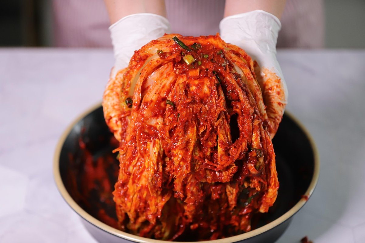 Le geste ancestral du kimchi Un gros plan sur la fabrication du kimchi, où des mains gantées manipulent une tête de chou chinois nappée de la fameuse pâte rouge épicée. Ce moment symbolise la transmission, le soin et la tradition autour de ce met fondamental de la culture coréenne.