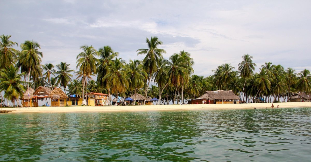 Plage de San Blas – Communauté Guna au Panama Vue d’une plage bordée de palmiers dans l’archipel de San Blas, Panama, avec des habitations traditionnelles de la communauté autochtone Guna.