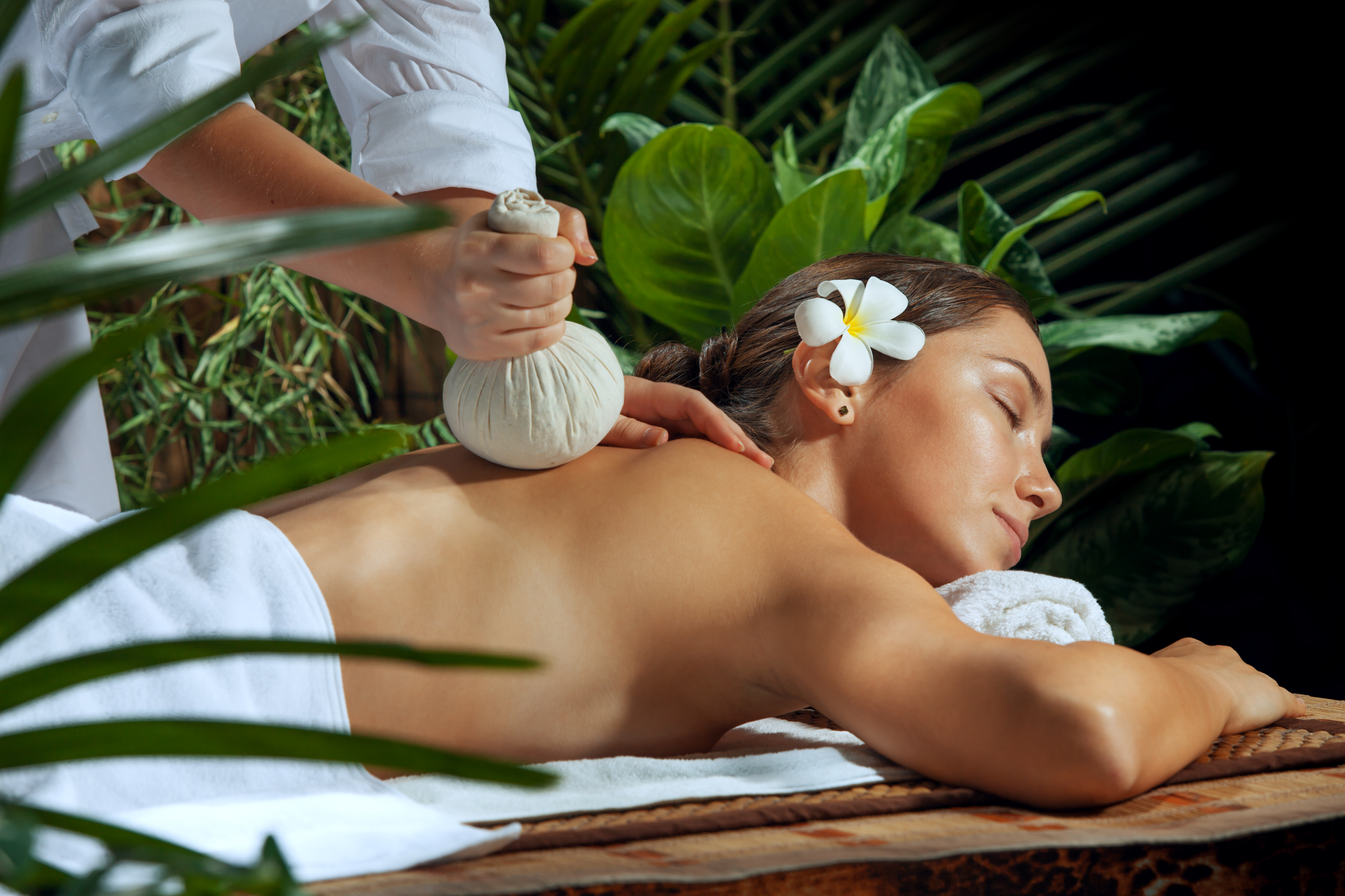 Rituel bien-être tropical – Massage aux plantes Femme recevant un massage aux plantes dans un spa tropical, symbole de détente et de rituels ancestraux de bien-être.