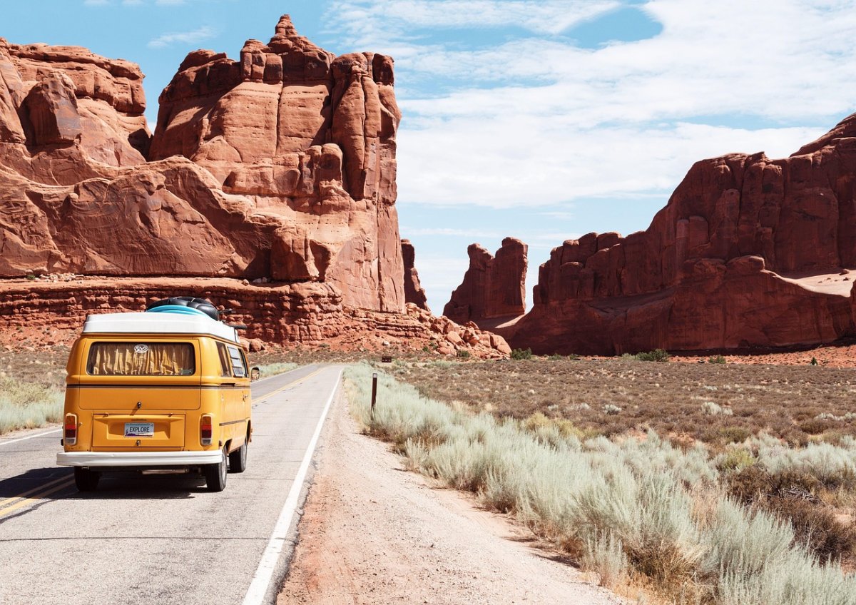 Voyage entre amis ou en famille – Road trip à travers les grands espaces Van jaune sur une route traversant des formations rocheuses rouges américaine, symbole de voyage en liberté entre amis ou en famille