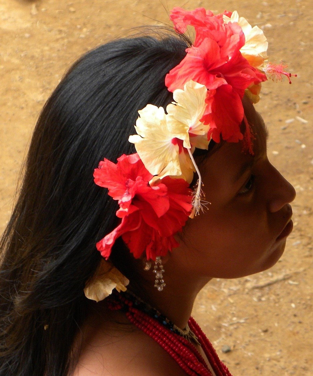 Jeune femme Guna avec coiffe traditionnelle en fleurs Portrait d’une jeune femme de la communauté Guna au Panama, portant une coiffe de fleurs d’hibiscus rouges et jaunes, un collier de perles et des boucles d’oreilles.